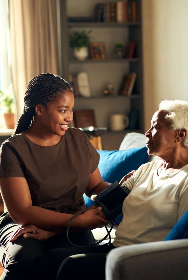 A caregiver takes an older woman’s blood pressure on her sofa